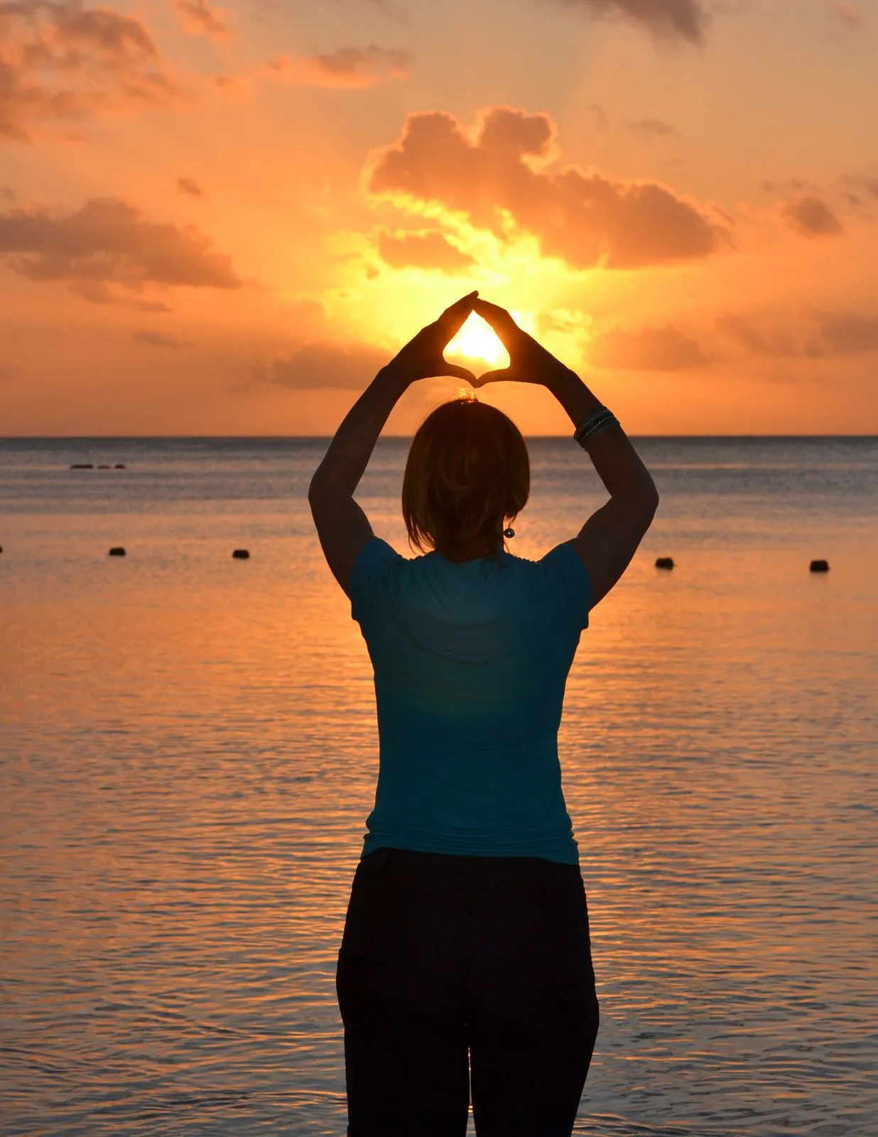Mujer de espaldas con los brazos elevados frente al mar al atardecer